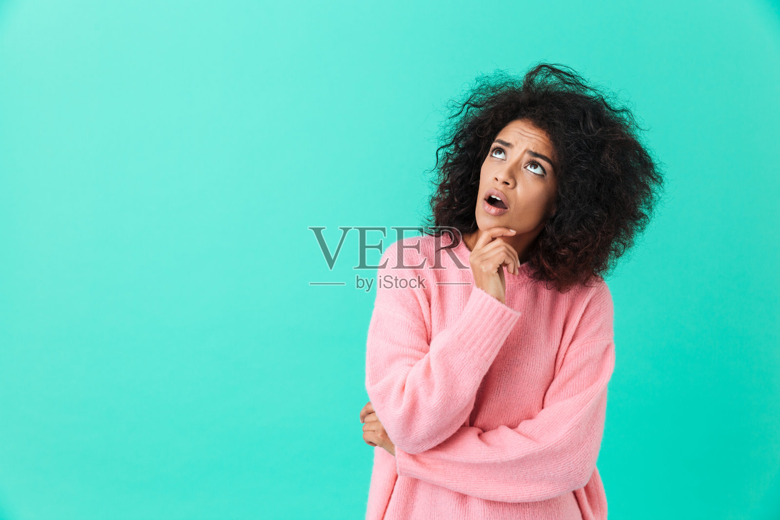 照片中,一个身穿粉色衬衫的黑发女子抬头看着文案空间,脸上带着兴趣,孤立在蓝色背景下照片摄影图片