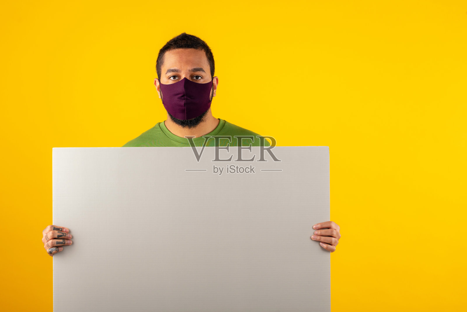 一名年轻男子的肖像戴着口罩,手持空白海报,背景为橙色照片摄影图片