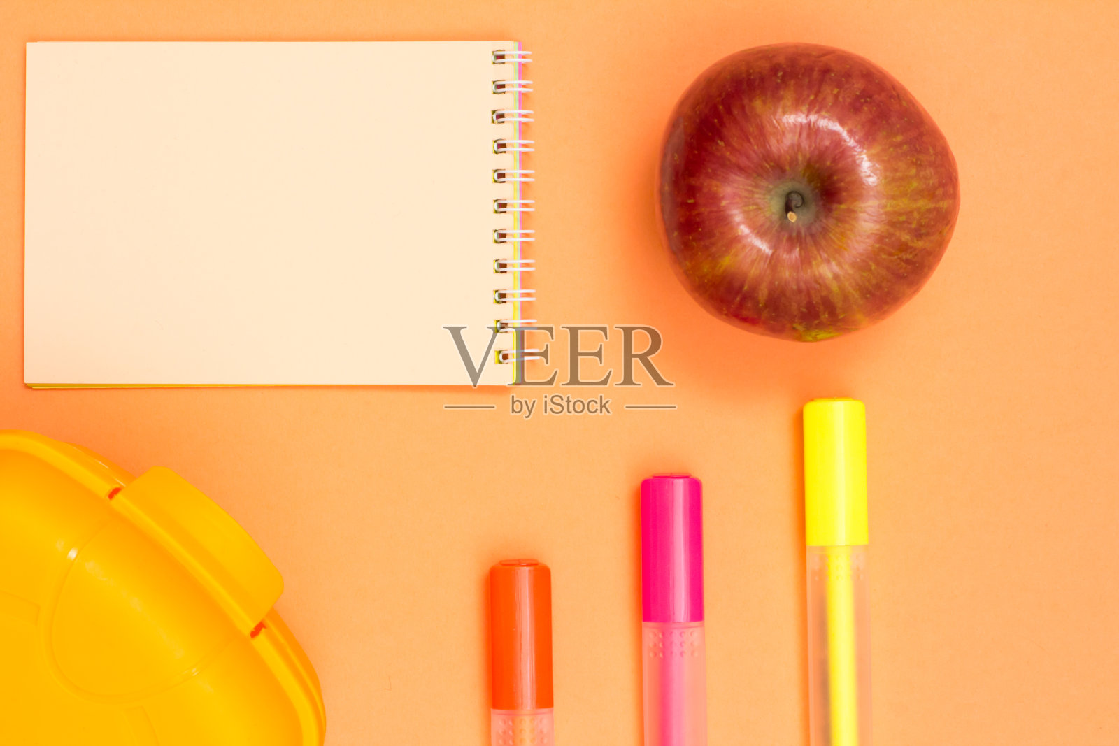 苹果,笔记本,彩色毛毡笔和粉红色背景的午餐盒照片摄影图片