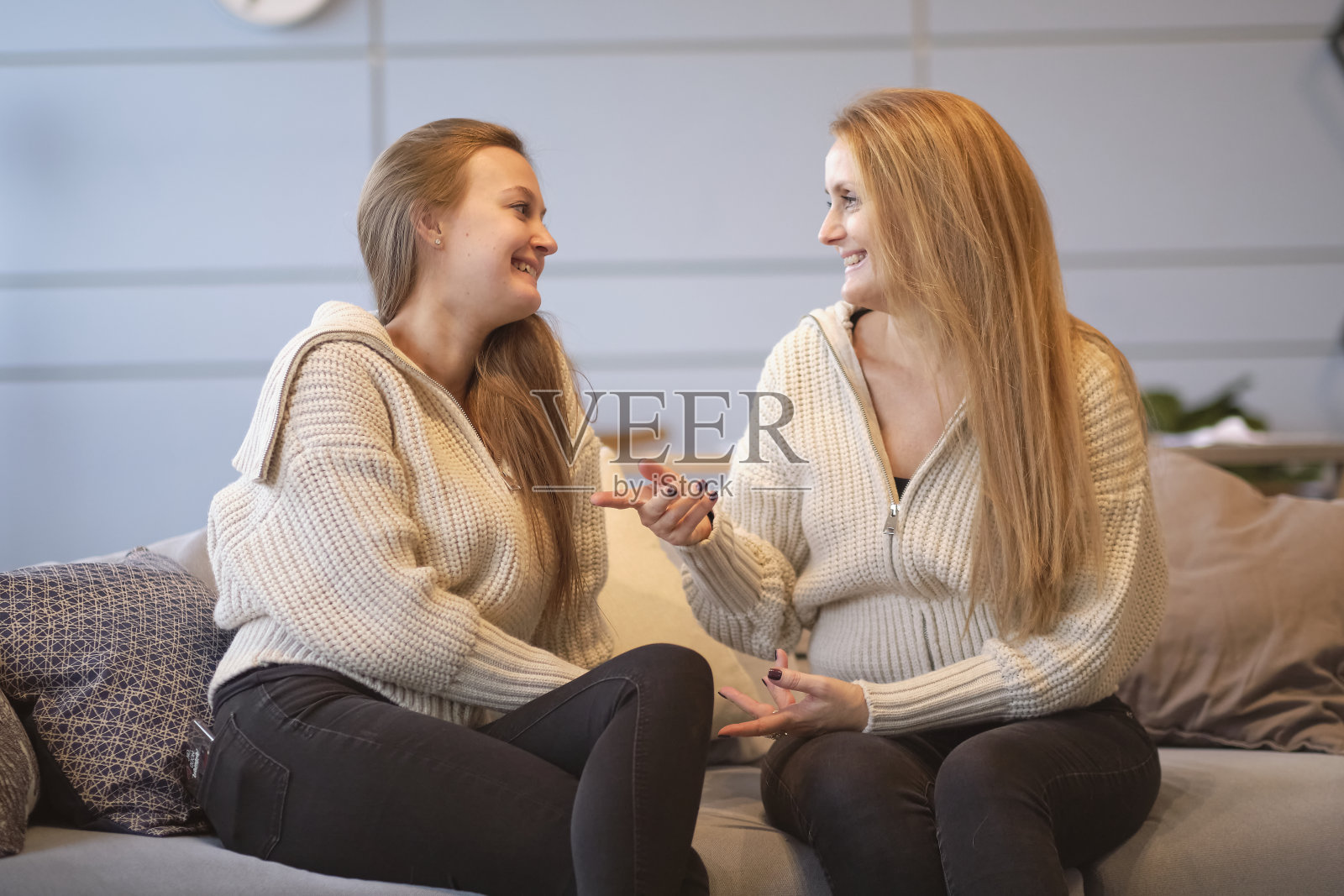 在家里的客厅里,一个快乐的年轻女子拥抱着年迈的母亲,坐在沙发上休息。快乐的妈妈和友好的女儿牵着手看着对方照片摄影图片