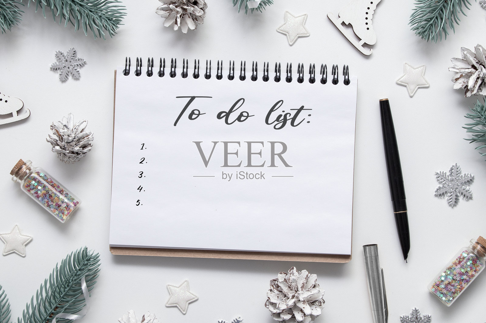 在平铺着冬季装饰的桌子上,用一个螺旋形记事本记录待办事项照片摄影图片