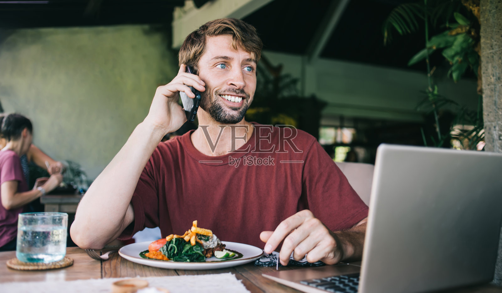 微笑的白人潮人20多岁坐在咖啡馆内部用手机聊天在自助餐厅吃午餐,积极的男性自由职业者在休息时打智能手机享受披萨照片摄影图片