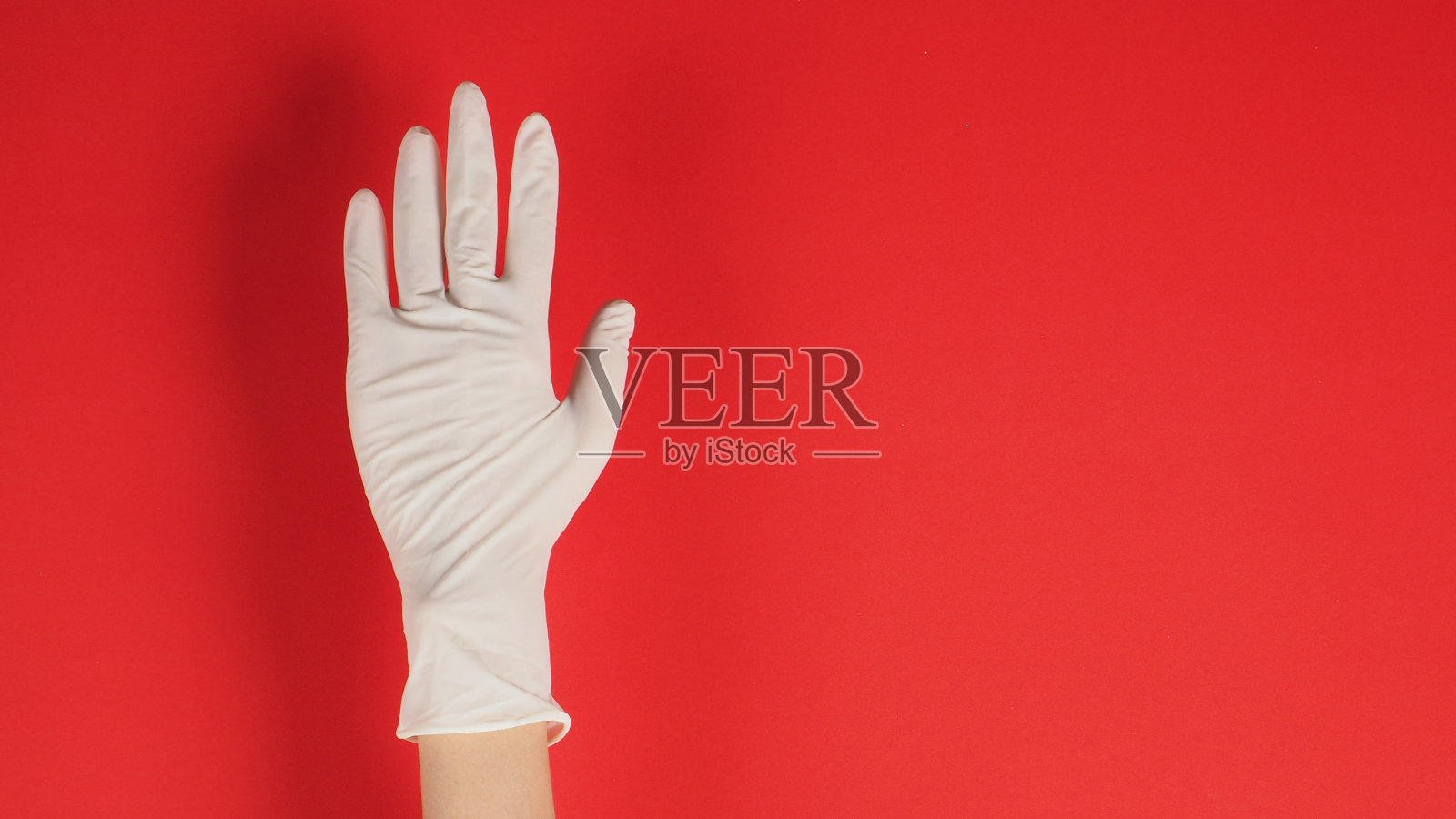 空手,右手戴白色乳胶手套,红色背景。照片摄影图片