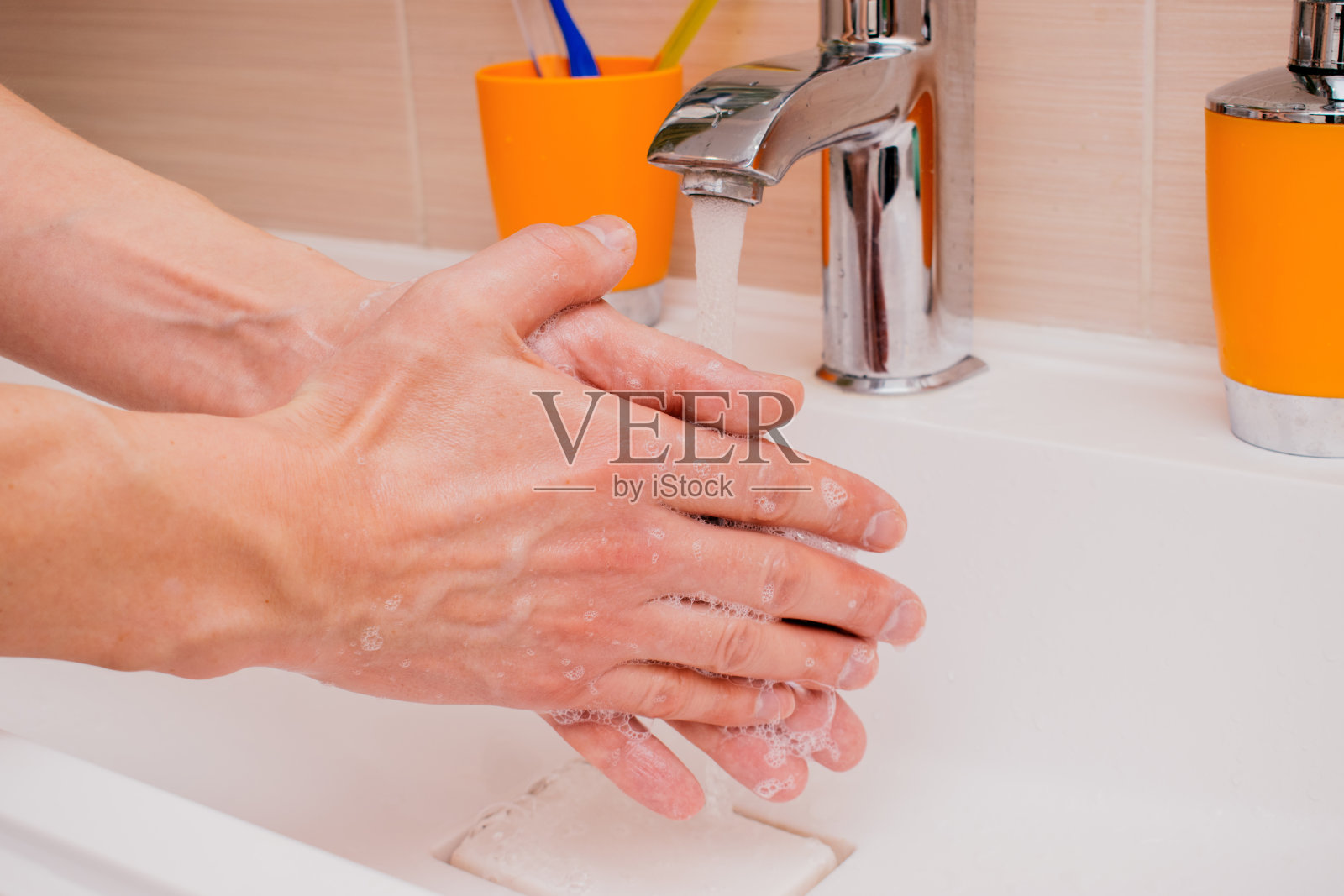 男子正用洗手液在水龙头下用水洗手,以预防冠状病毒感染,树立卫生观念。有选择性的重点照片摄影图片