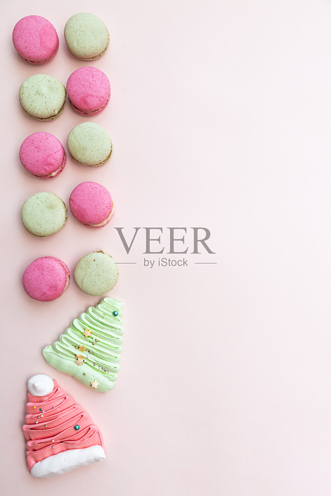 粉色和绿色的马卡龙,浅粉色的桌子上放着蛋白霜和糖果。糖果的背景。节日的概念照片摄影图片