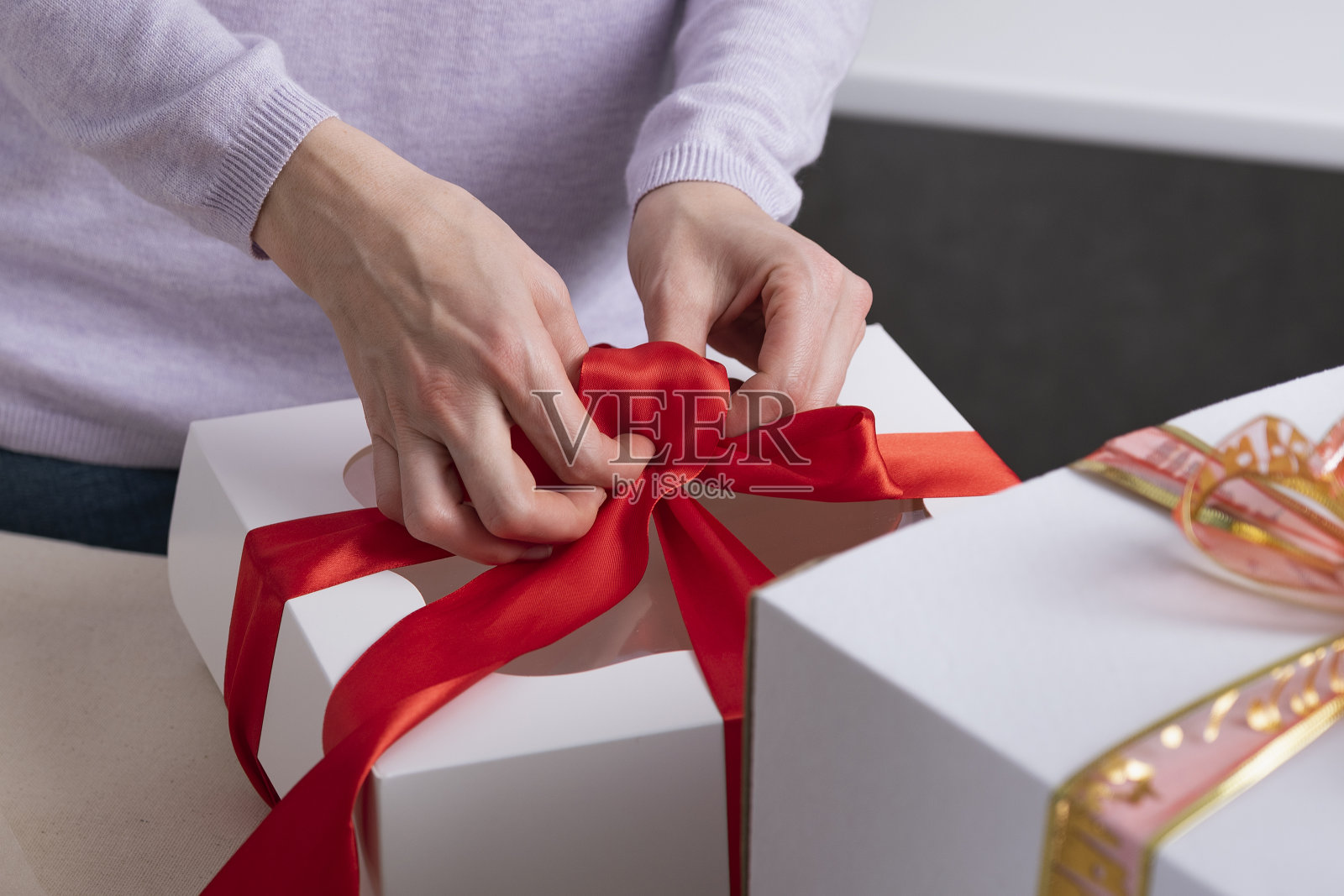 女人在包装礼物。带红丝带的白色盒子。照片摄影图片