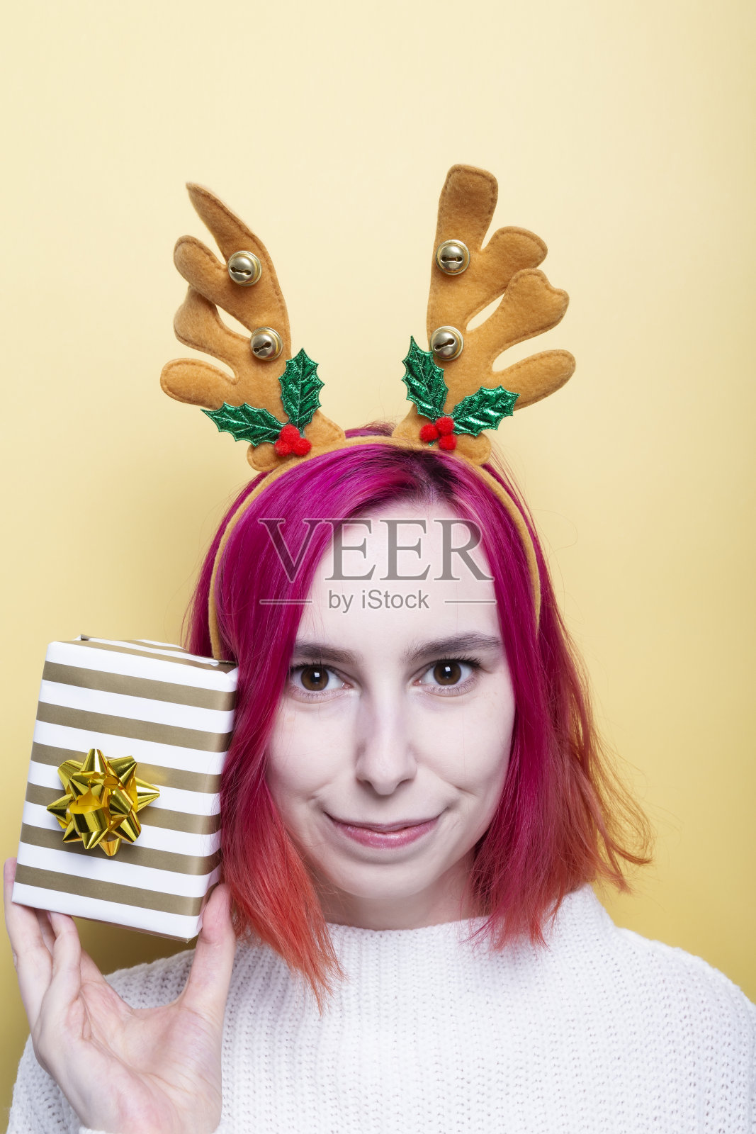 女孩穿着白色的毛衣,头上戴着鹿角,手里拿着礼物,黄色的背景照片摄影图片