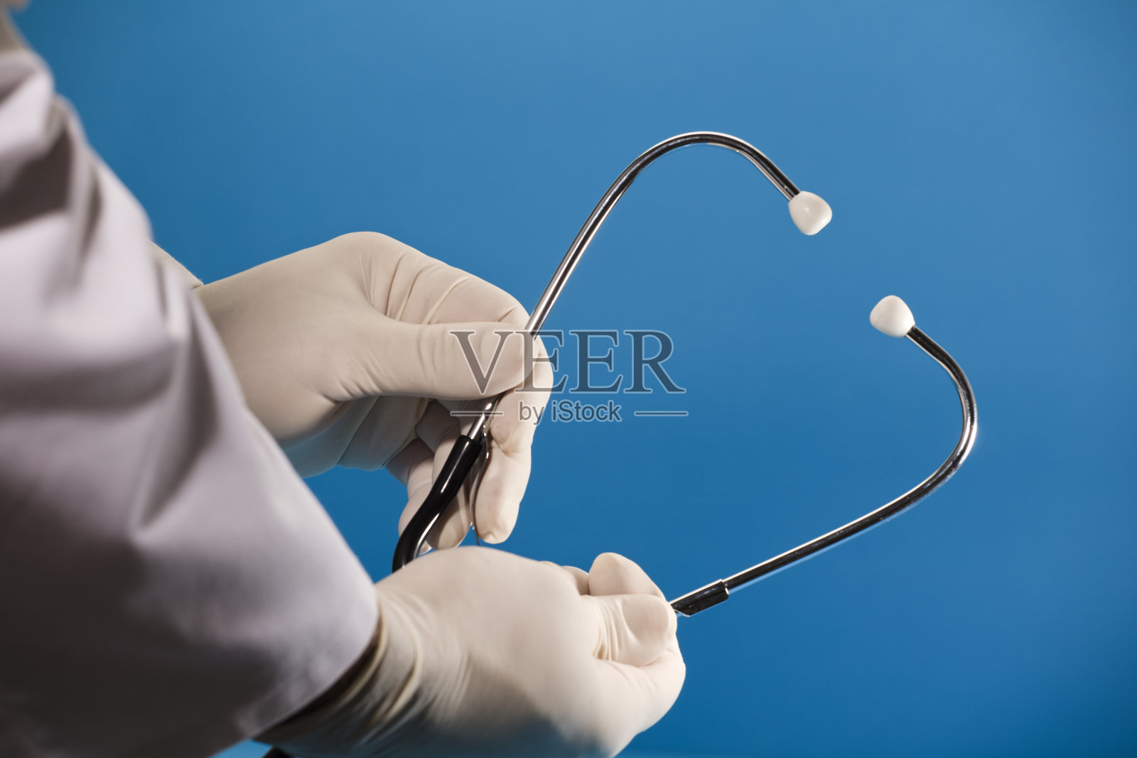 医生手持听诊器,手术手套,蓝色背景。照片摄影图片