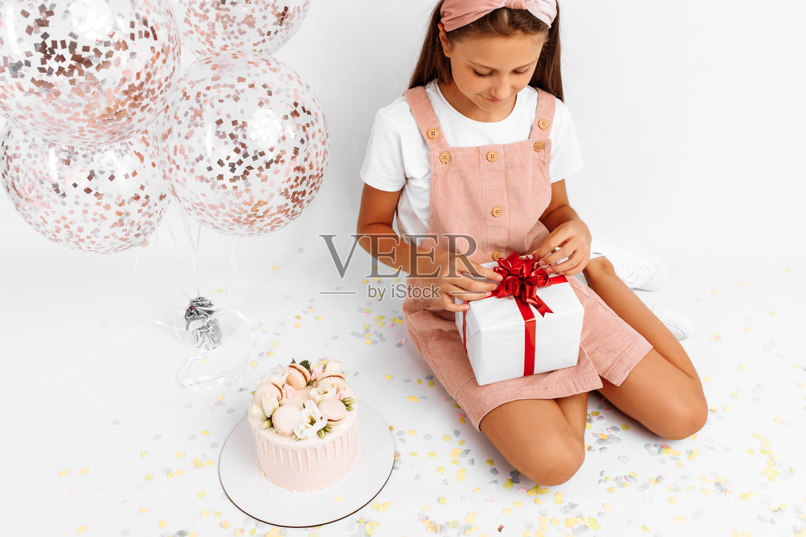 快乐的小女孩,拿着气球,漂亮的大蛋糕和礼物,坐在白色的背景上照片摄影图片