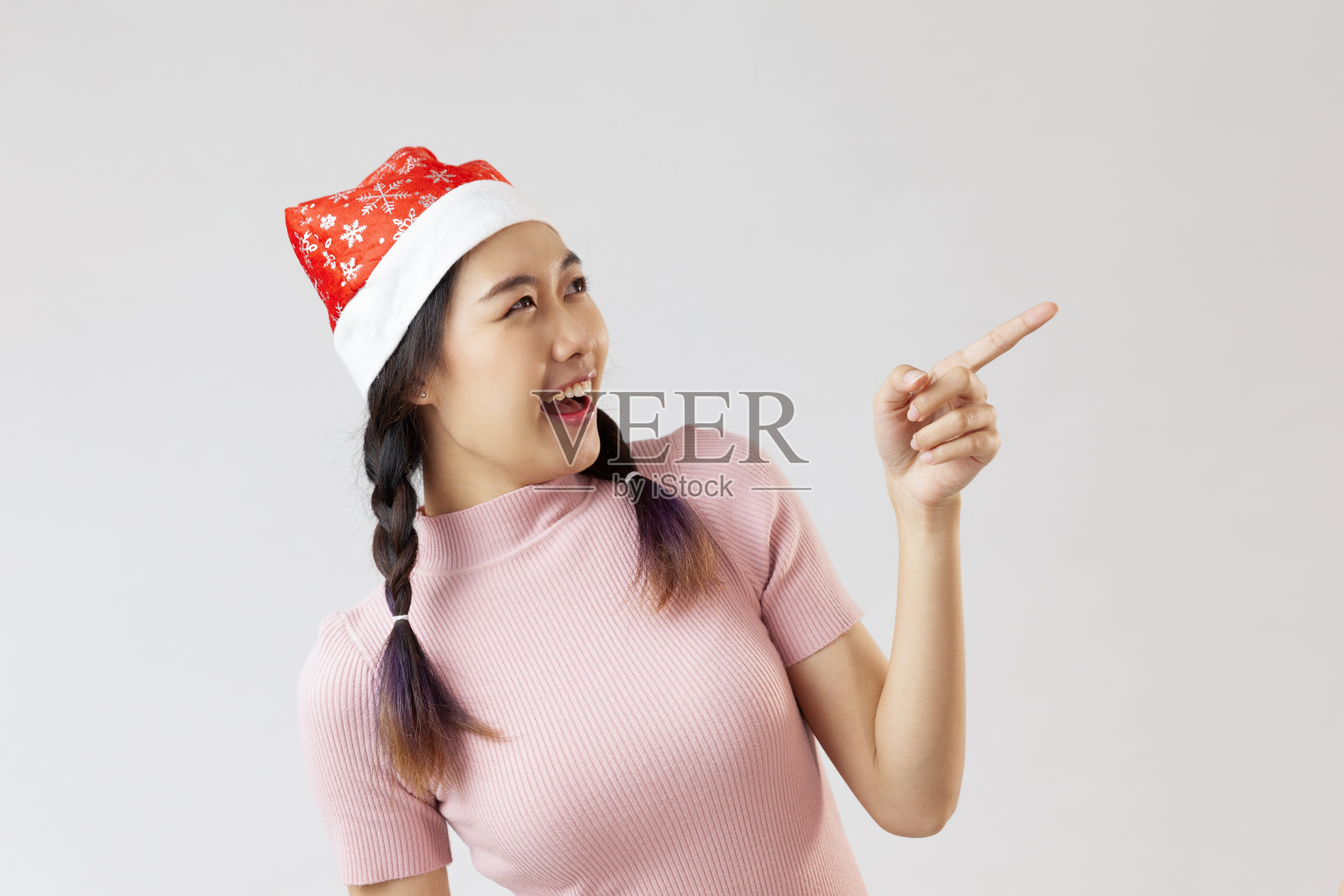 年轻的亚洲女性戴着圣诞老人的帽子和粉红色的衬衫。站着,手指向右侧照片摄影图片