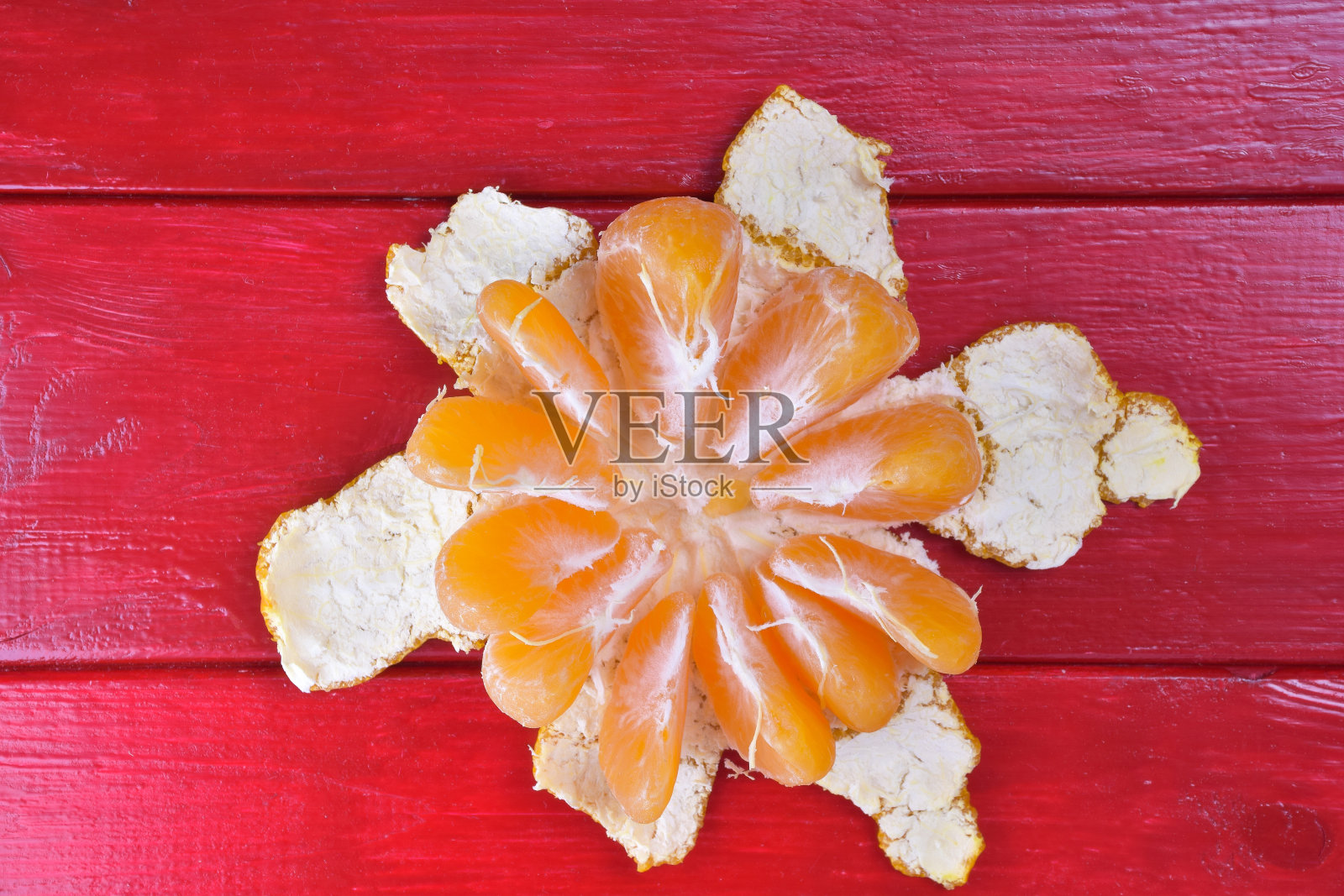 一个去了一半皮的橘子躺在框架中央的红色木制背景上照片摄影图片