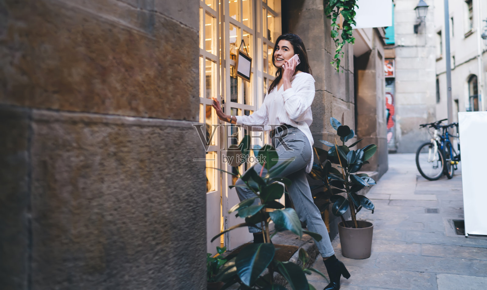 快乐的女性用户打电话给最好的朋友讨论购物时间,同时打开门与模拟招牌时装店,快乐的时髦女孩20多岁享受手机通信照片摄影图片