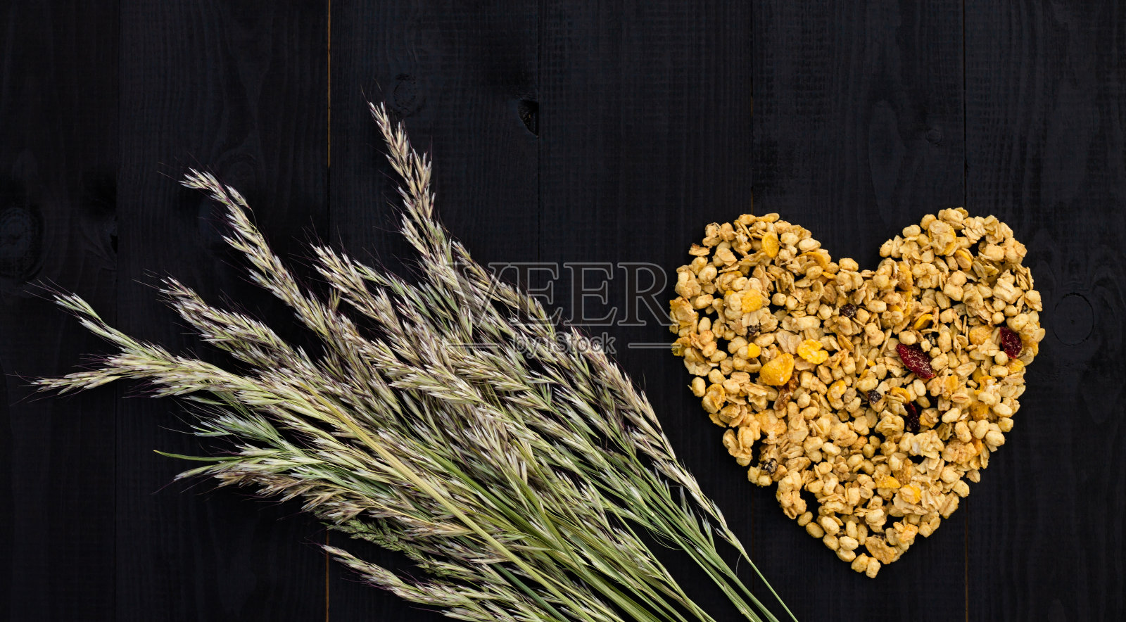 心脏布局的格兰诺拉麦片和小穗在黑色木质背景。平的。副本的空间。照片摄影图片