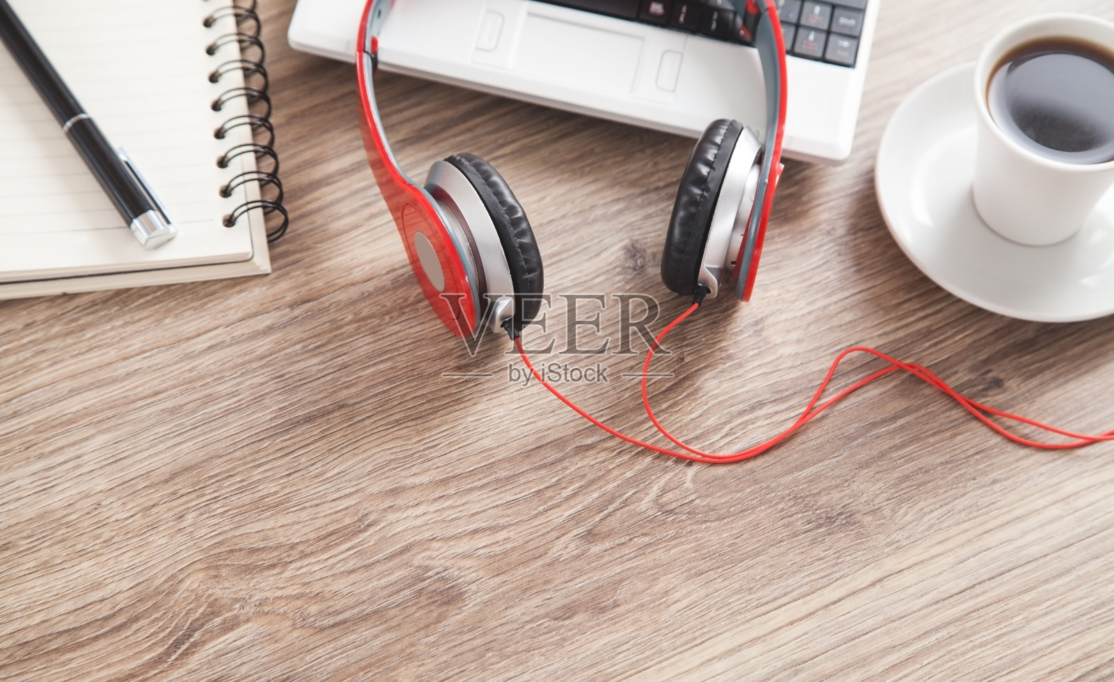 红色耳机,咖啡,电脑键盘,笔和笔记本放在木桌上。照片摄影图片