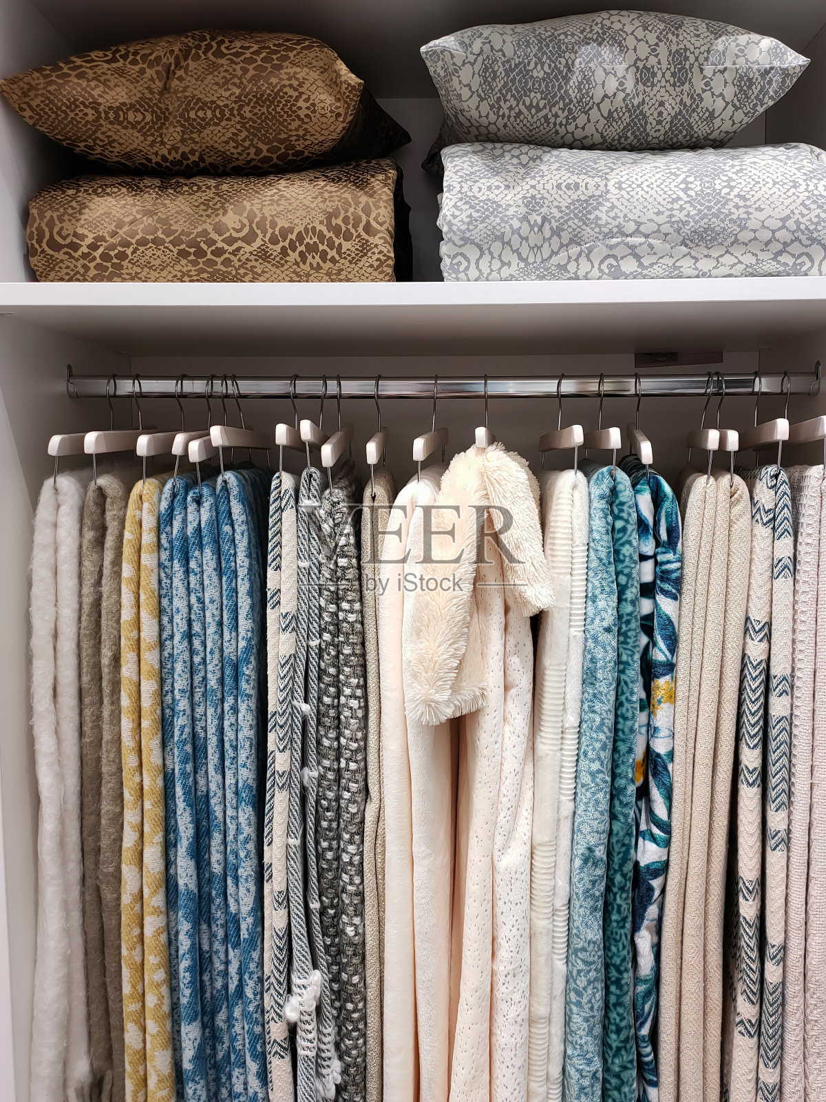 衣橱的视图,毛毯挂在衣架上,枕头和毯子在架子上照片摄影图片