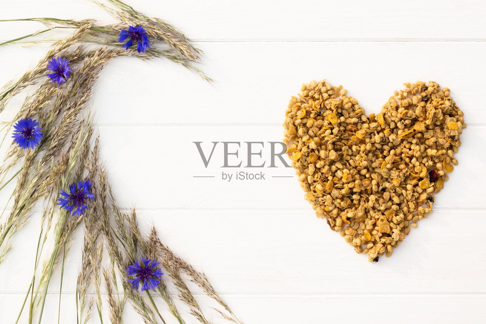 在白色的木质背景上,麦片、小穗和矢车菊的心形图案。平的。副本的空间。照片摄影图片
