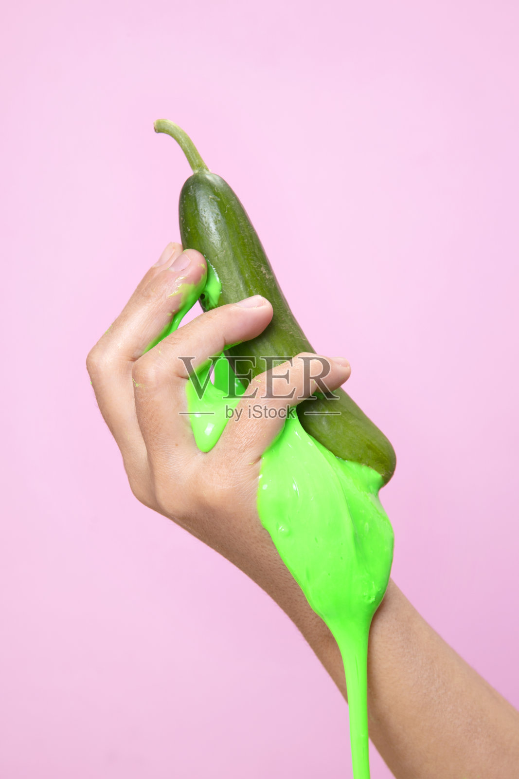 手握绿色的有机黄瓜片在粉红色的纸背景上。照片摄影图片