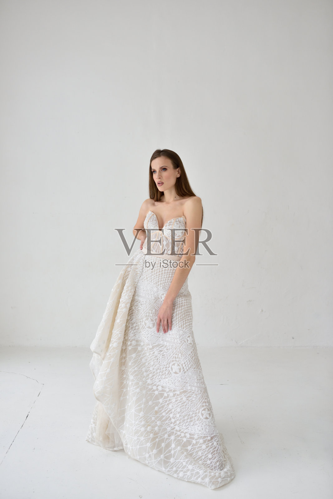 一个美丽的新娘穿着婚纱站在一个白色的工作室,在茁壮成长和看向一边照片摄影图片