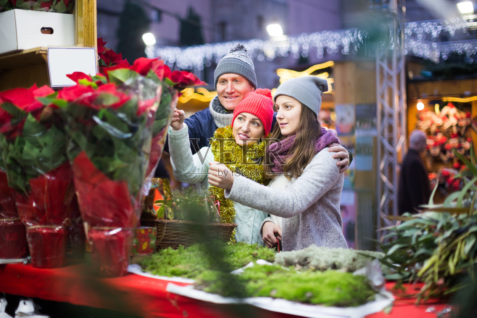 快乐的妈妈,爸爸和十几岁的女孩在圣诞集市上买红色的大戟和鲜花装饰照片摄影图片