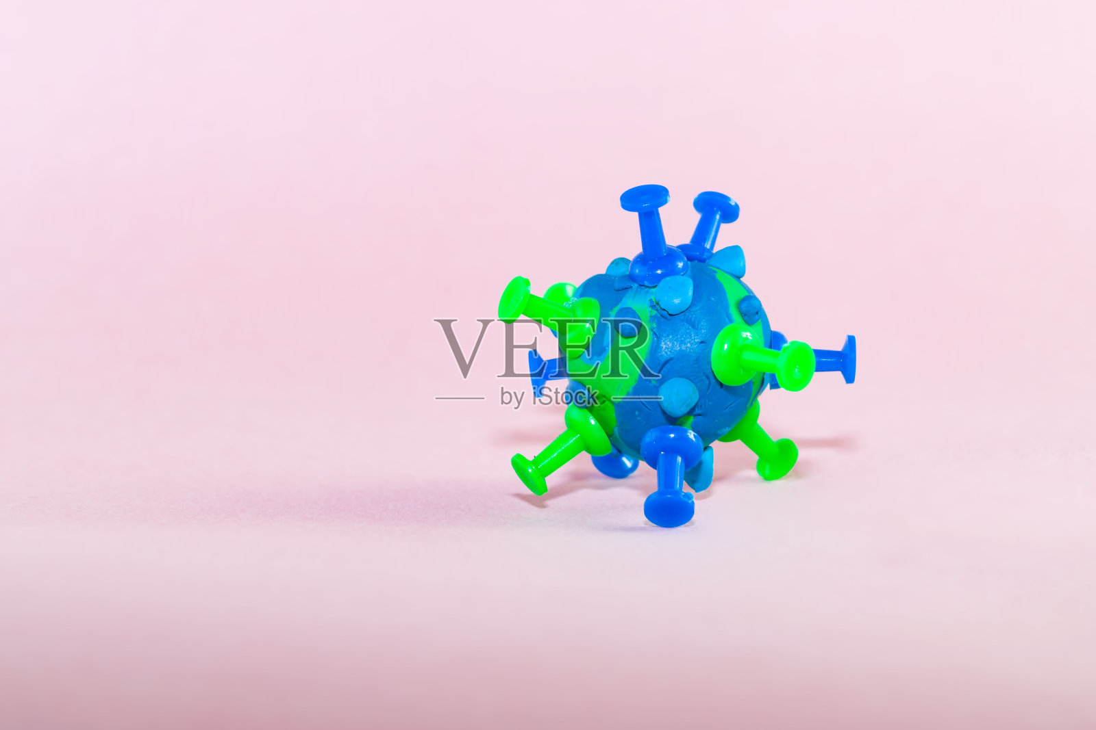 一个冠状病毒细菌模型,由蓝绿色的橡皮泥在粉红色的纸背景。主题防护、病毒传播和疫情危害。冠状病毒,ncov-19照片摄影图片
