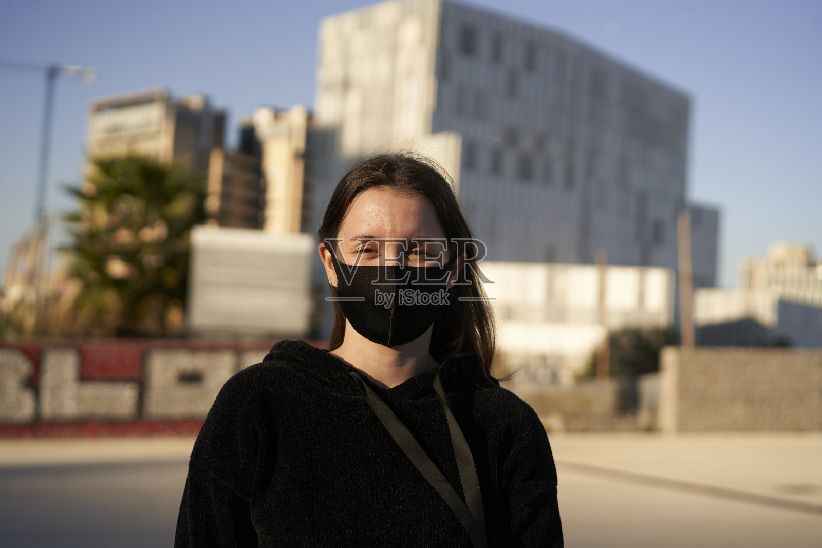 看着摄像机。一幅因冠状病毒大流行而戴口罩的西班牙裔年轻女孩的肖像。她在一个城市里。衣服和面具都是黑色的。照片摄影图片