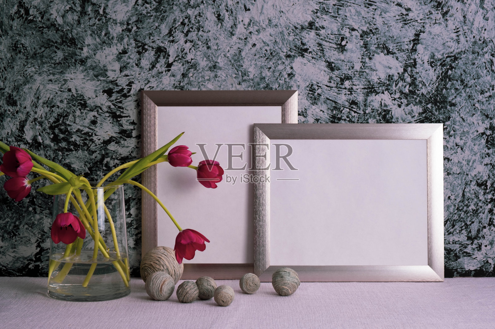 玻璃花瓶里放着红色郁金香,桌子上放着灰色背景上的灰色相框照片摄影图片
