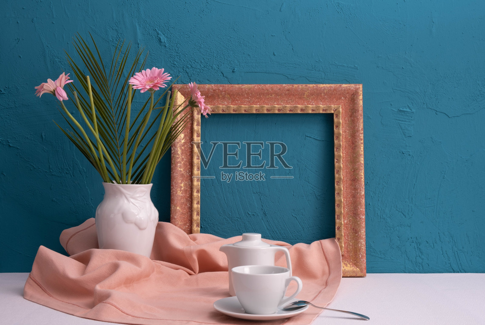 金色的画框,一个咖啡杯,一个茶壶,还有一个蓝色背景上的非洲菊花瓶照片摄影图片