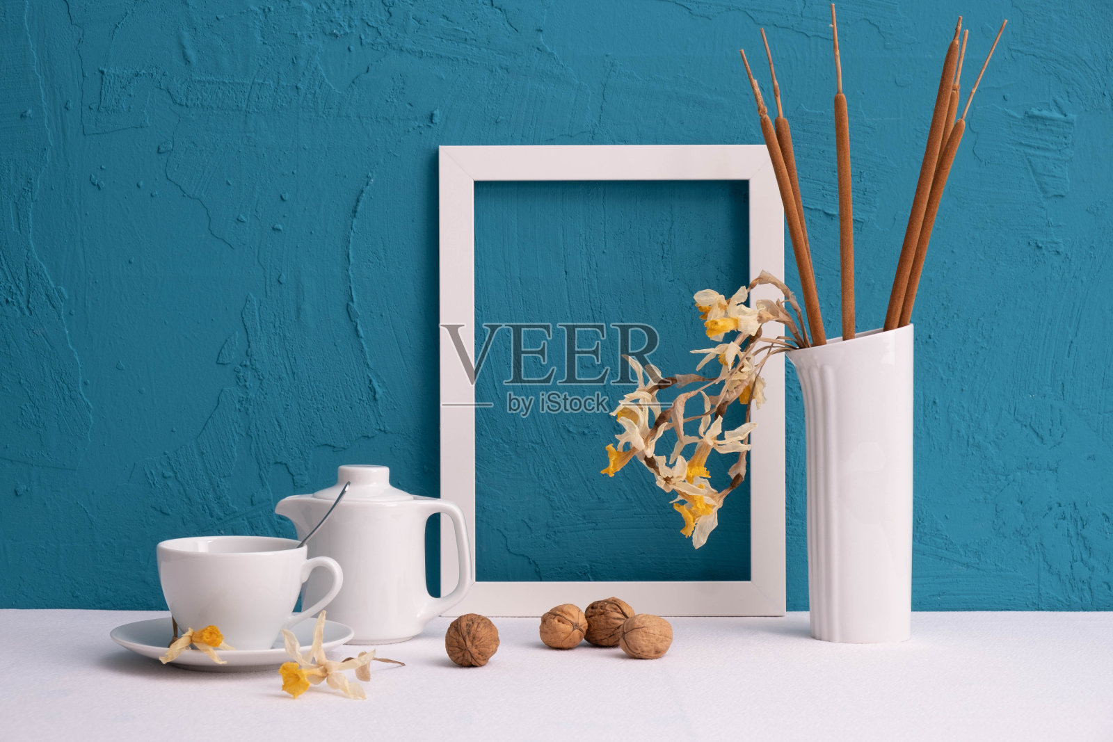 白色花瓶,芦苇锥,相框,核桃,咖啡杯和茶壶在蓝色背景的桌子上照片摄影图片
