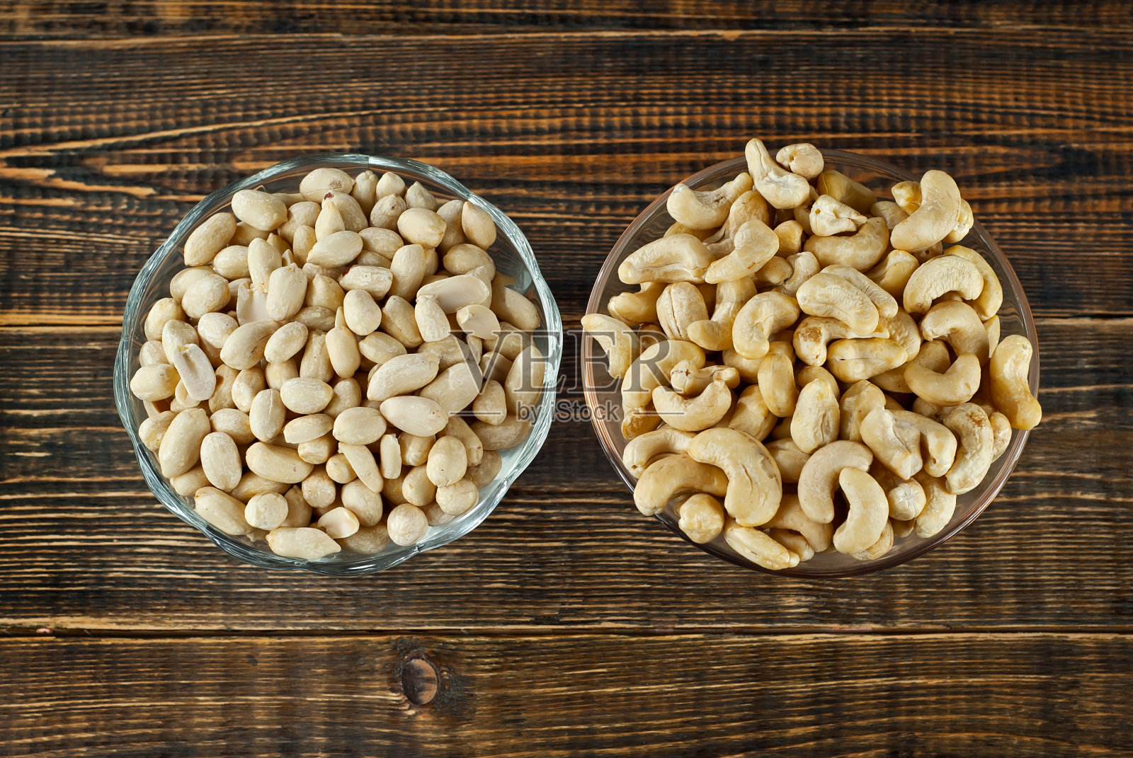 花生和腰果放在一个干净的玻璃碗里,放在一块破旧的木板上。棕色的木桌上放着坚果。照片摄影图片