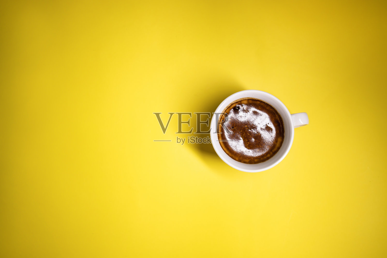 一杯黄色背景的咖啡。一杯满杯的浓咖啡,背景是黄色的彩色纸,从上面俯瞰照片摄影图片