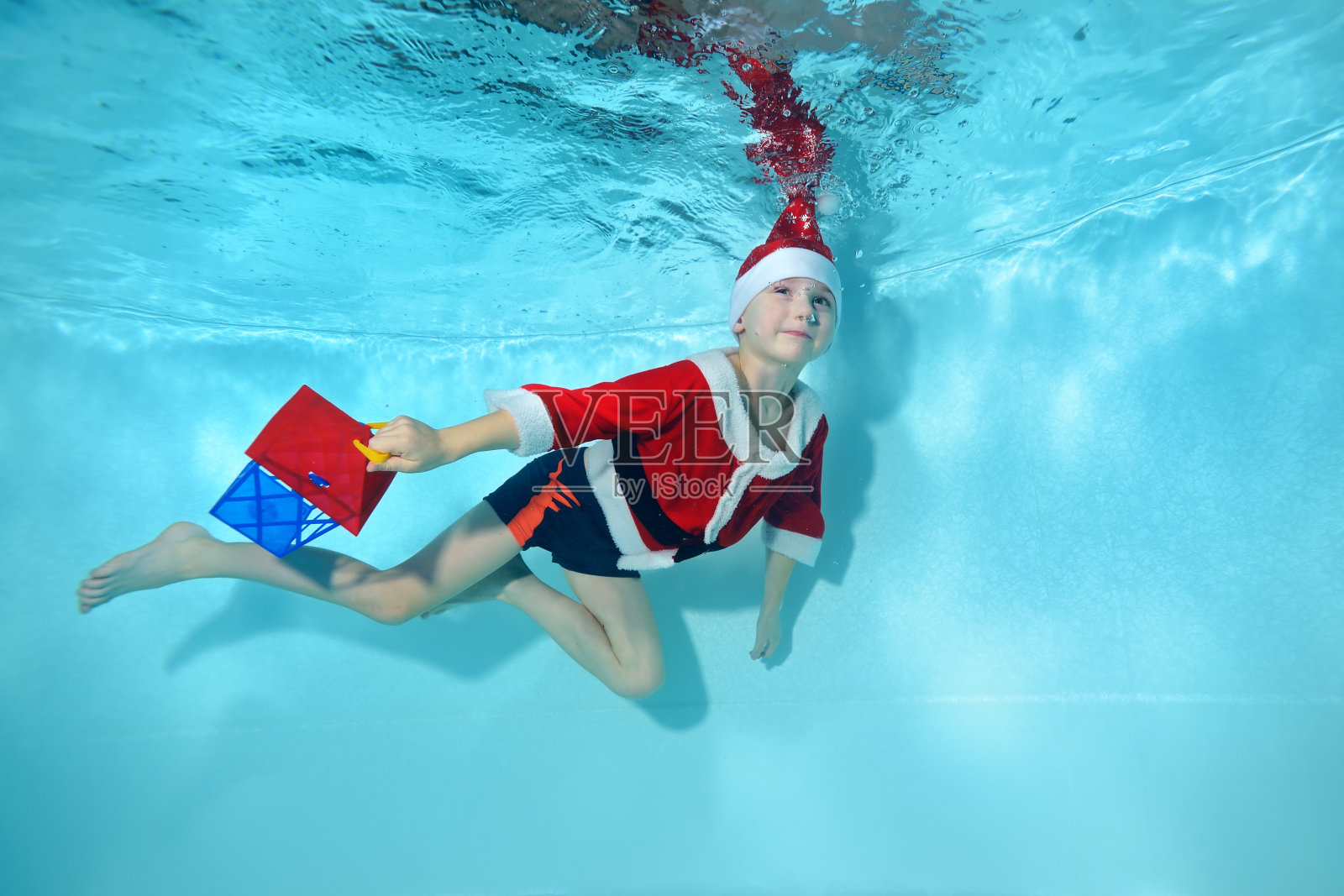 一个健壮的小男孩穿着圣诞老人的服装在游泳池里游泳。游泳课。健康的生活方式。庆祝的概念。照片摄影图片