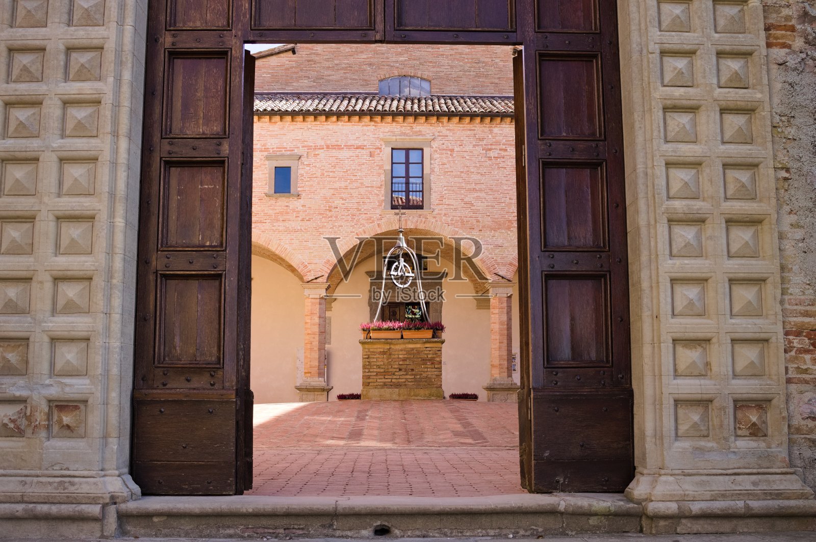 中世纪修道院入口的旧木门,院子里有一口砖井(意大利翁布里亚古比奥)照片摄影图片