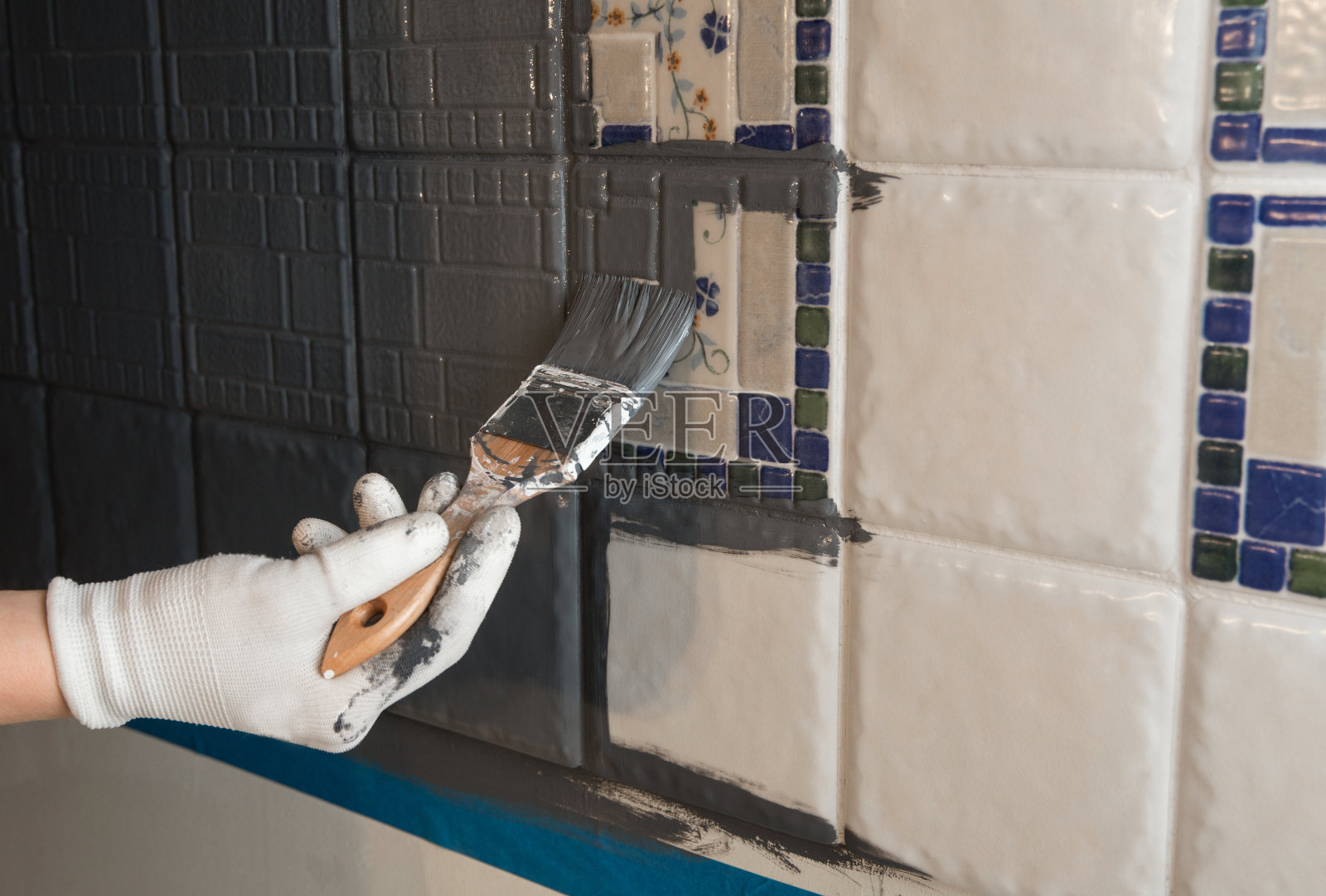 在家里用现代灰色粉笔油漆重新粉刷旧式厨房瓷砖后墙。给老厨房新的外观概念。手持画笔工具。照片摄影图片