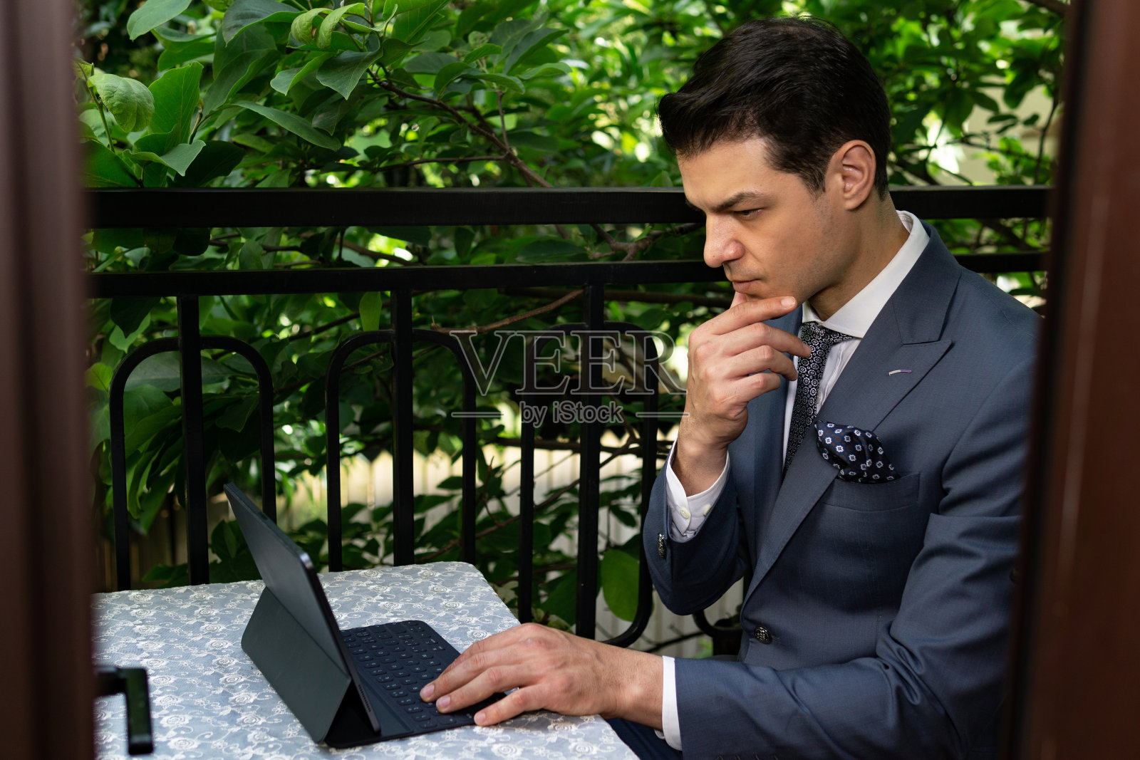 英俊的成功男人坐在美丽的阳台上,在电脑上工作。照片摄影图片