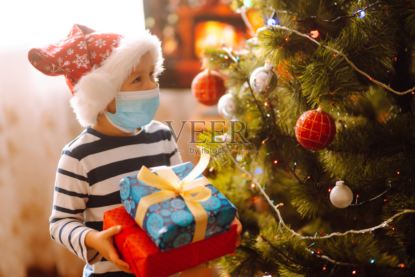 快乐的孩子在无菌医疗面具拿着圣诞礼物。照片摄影图片