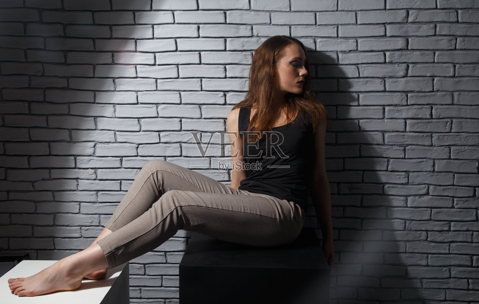 在砖墙背景上坐着的女人看着一边的照片照片摄影图片