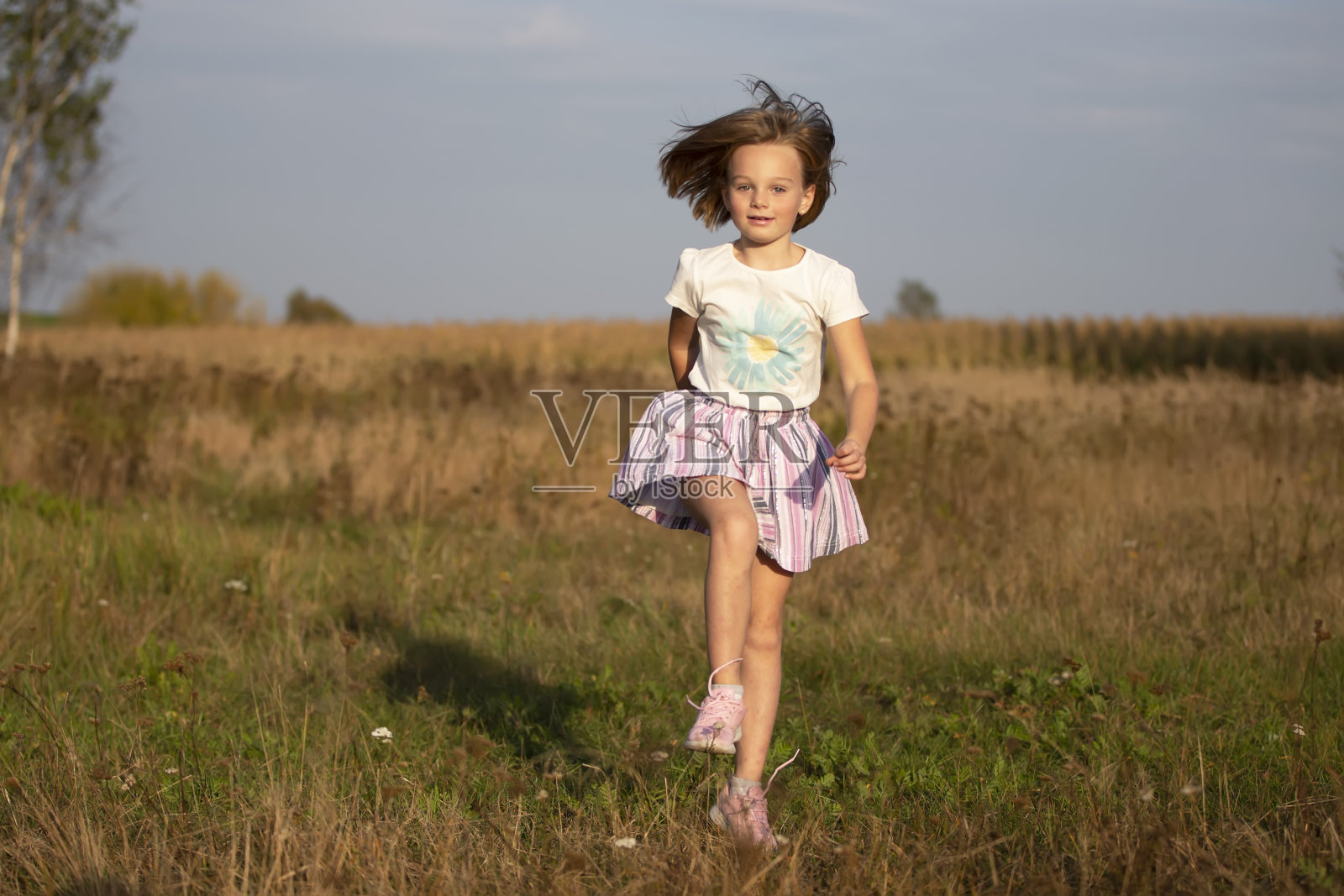 美丽的小女孩在夏天的田野里奔跑。孩子在草地上玩耍。照片摄影图片