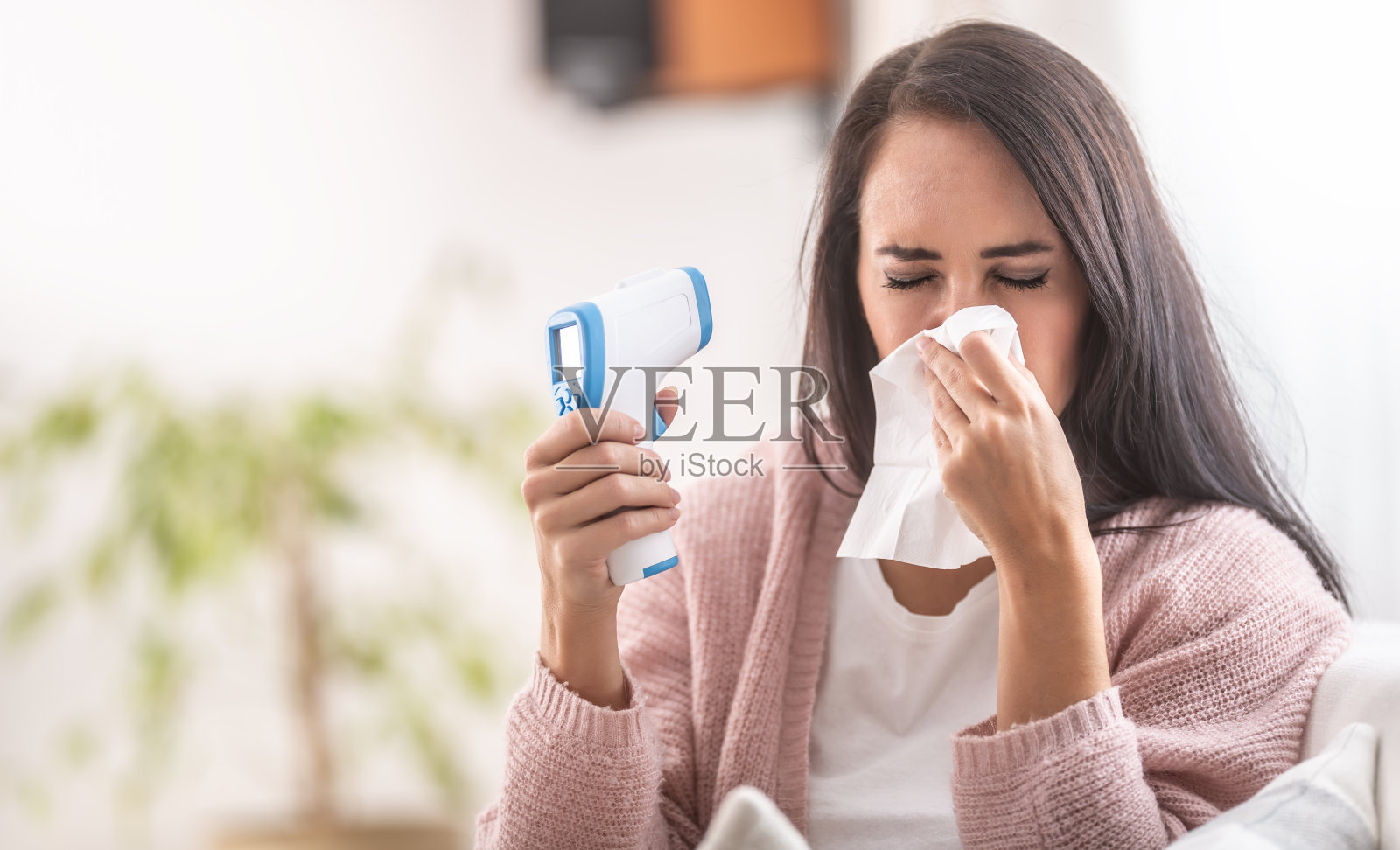 一名女子对着一张纸巾打喷嚏,纸巾上拿着红外线额头温度计。照片摄影图片