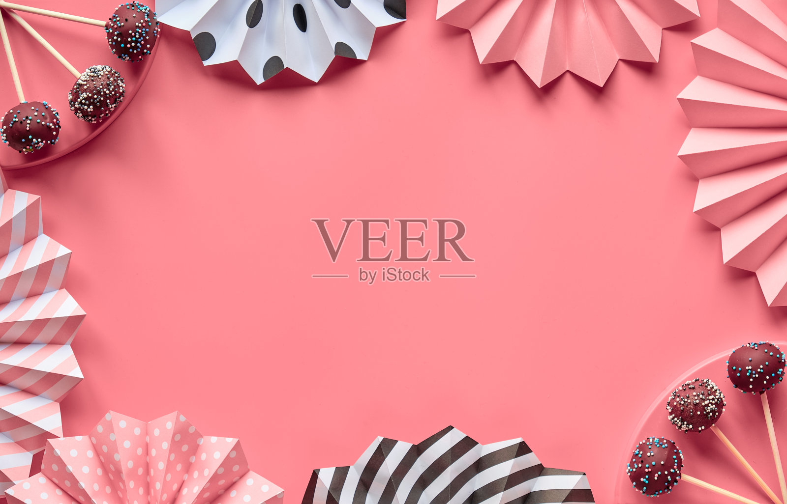 带有文本空间的装饰性框架。蛋糕棒棒糖覆盖着巧克力和彩色糖霜。创意的单色平铺在粉红色的纸上,上面装饰着美味的流行蛋糕,折叠的纸扇照片摄影图片