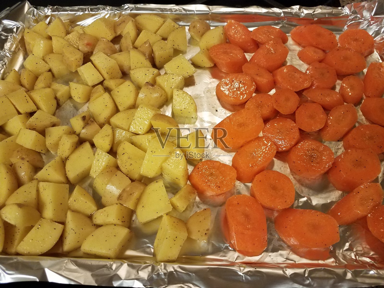 土豆和胡萝卜放在烤盘上,用箔纸包裹照片摄影图片