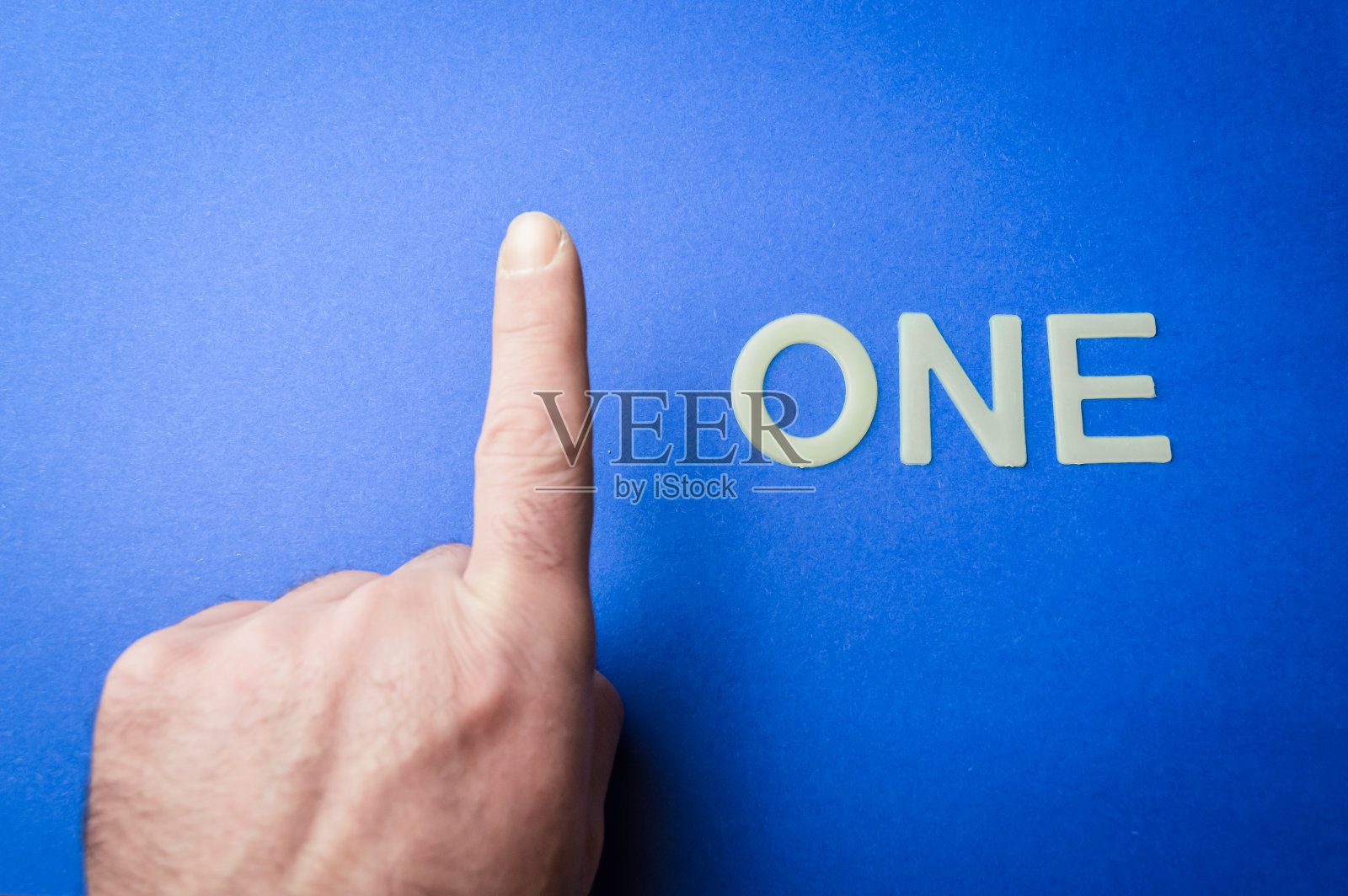 人类手指旁边用塑料字母在蓝色纸背景上写的“一”字,概念照片摄影图片