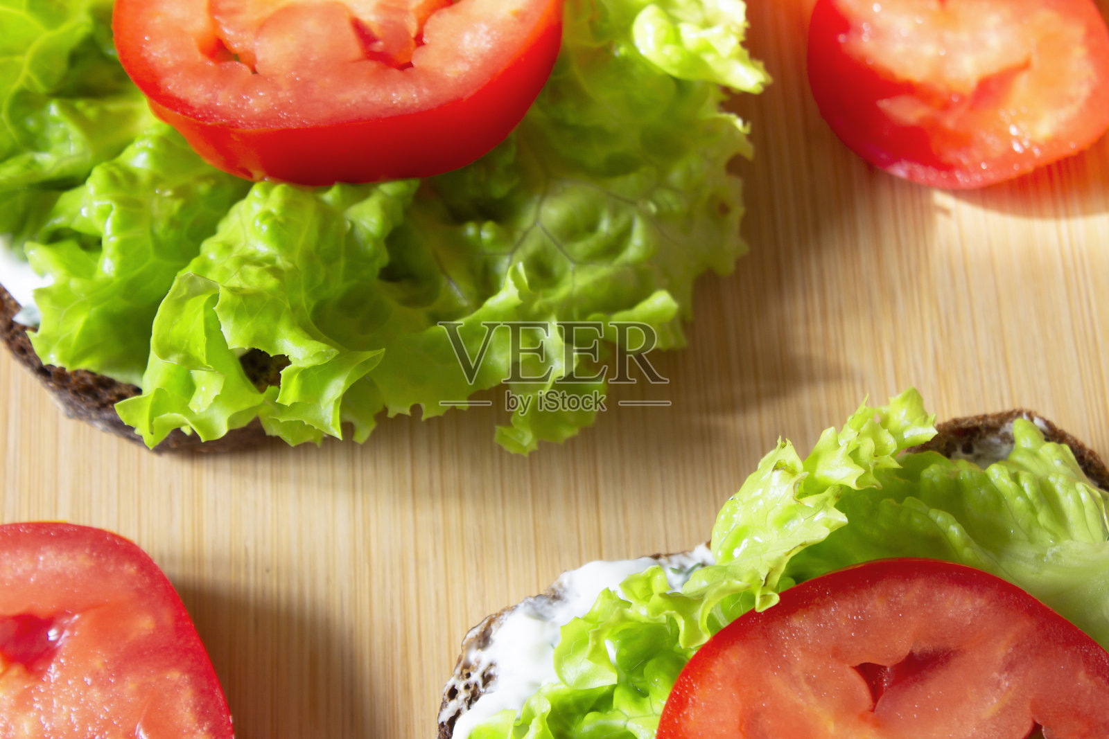 三明治配新鲜蔬菜。绿色沙拉,番茄,芝士酱,莳萝,全麦黑麦吐司,放在木板上。早餐概念为节食者,纯素食者,适当的营养。前视图。照片摄影图片