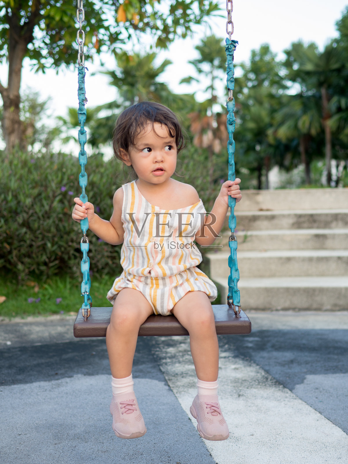 小女孩坐在操场的秋千上。照片摄影图片