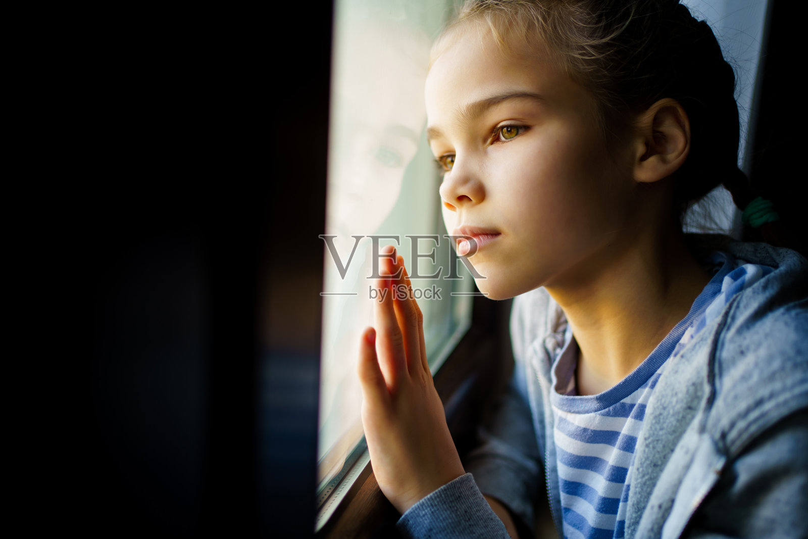 透过玻璃。悲伤的少女在窗外向外看。照片摄影图片