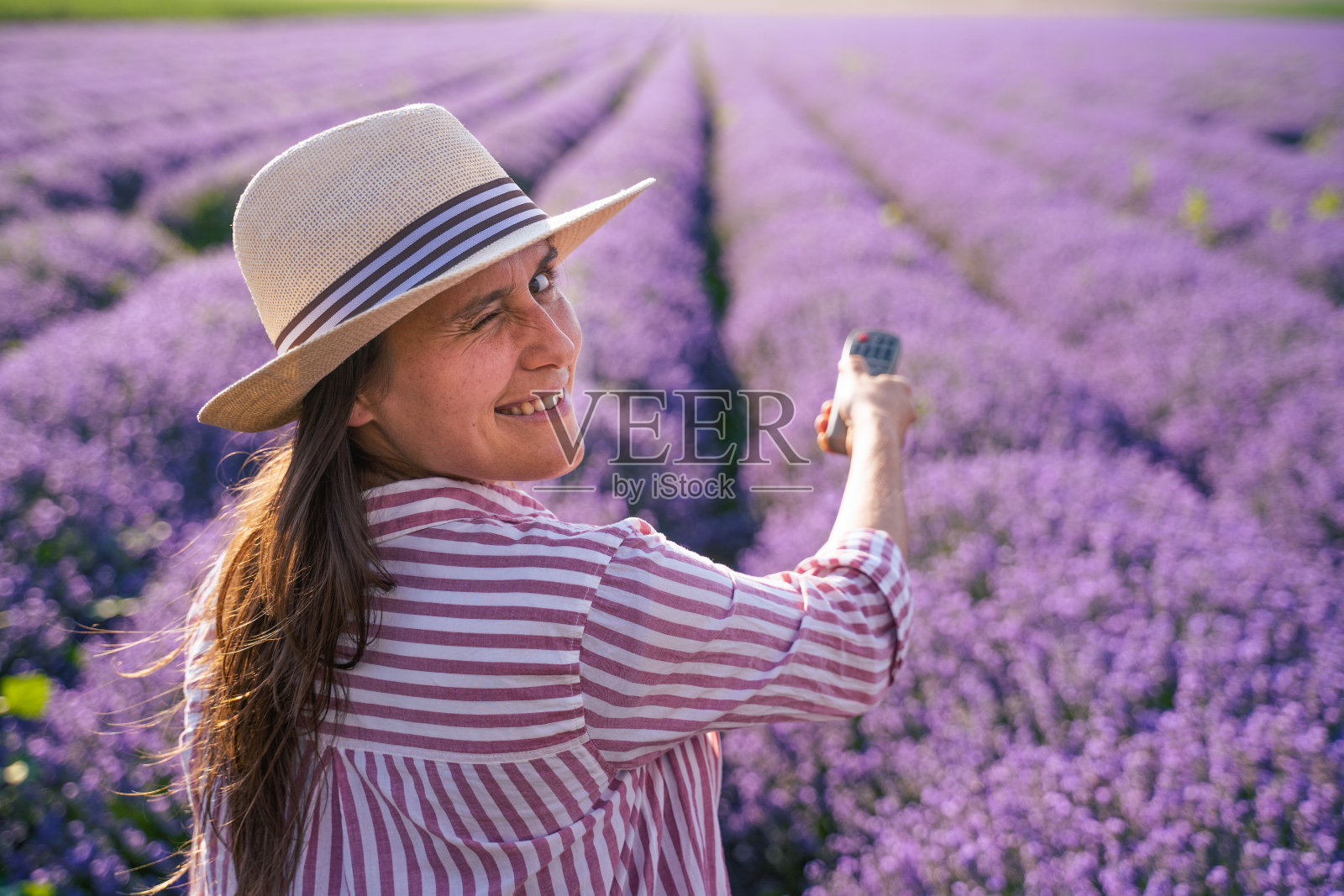 年轻女子用遥控器打开电视。这款全新巨大的4k智能oled电视画面令人惊叹。家庭影院。盛开的薰衣草田的壮丽景色。旅游热。照片摄影图片