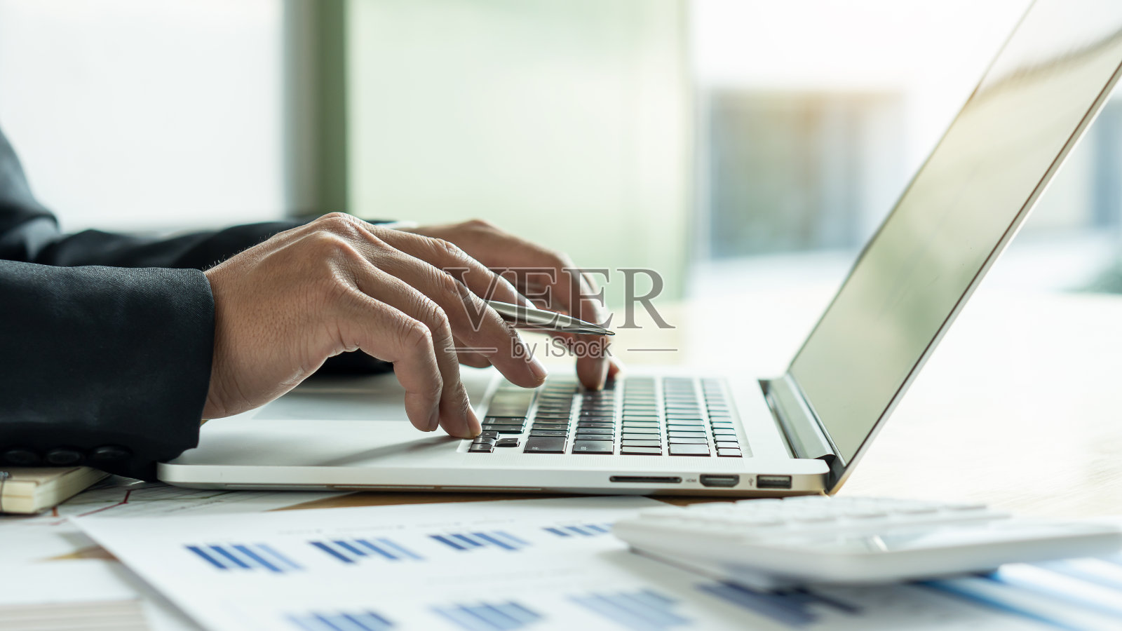 那只手握着笔,在桌子上用商人的笔记本电脑绘制图表照片摄影图片