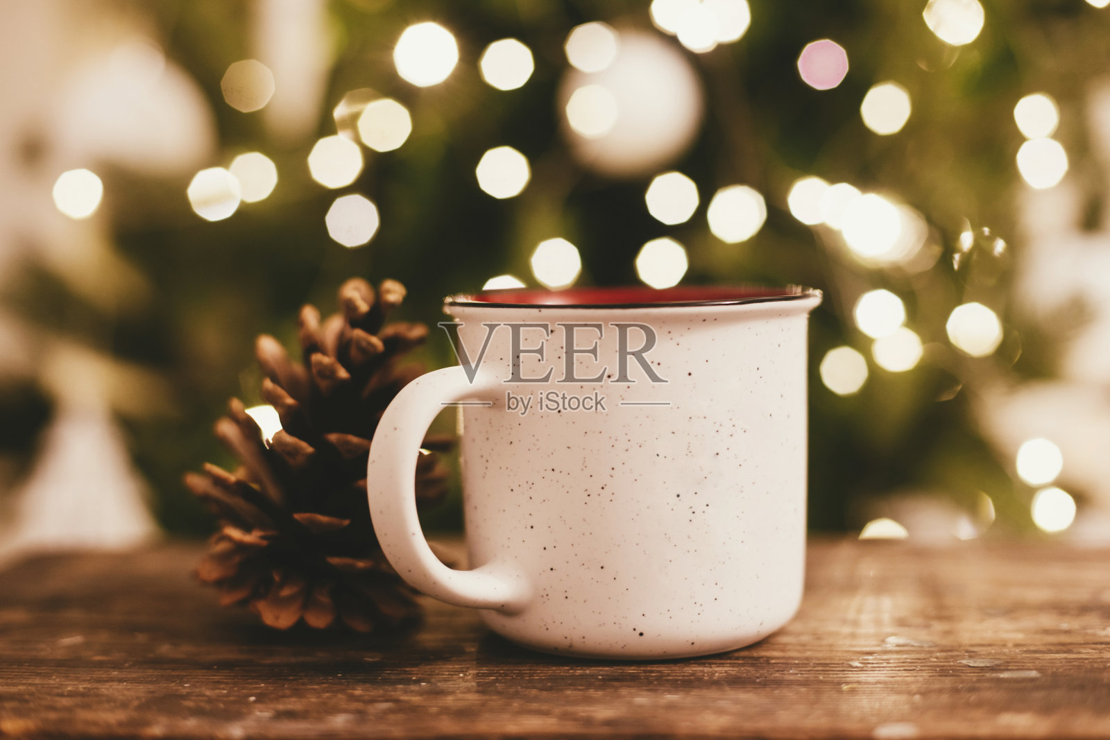 一杯茶和松果在质朴的木制背景下,在圣诞树灯焦。圣诞快乐,节日快乐!照片摄影图片