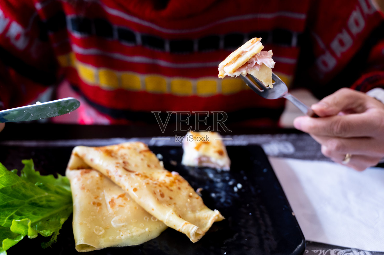 一个火腿和奶酪可丽饼配上生菜叶的特写镜头。这叉子有一口可以吃的东西。照片摄影图片