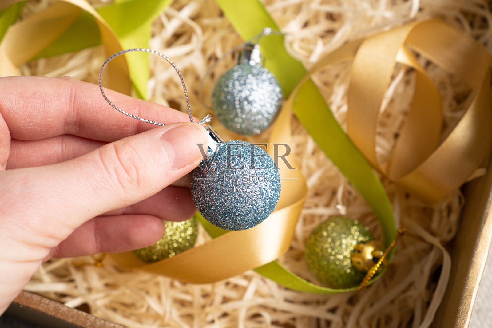 手拿着小闪亮的蓝色树装饰在干木丝上。圣诞树装饰品照片摄影图片