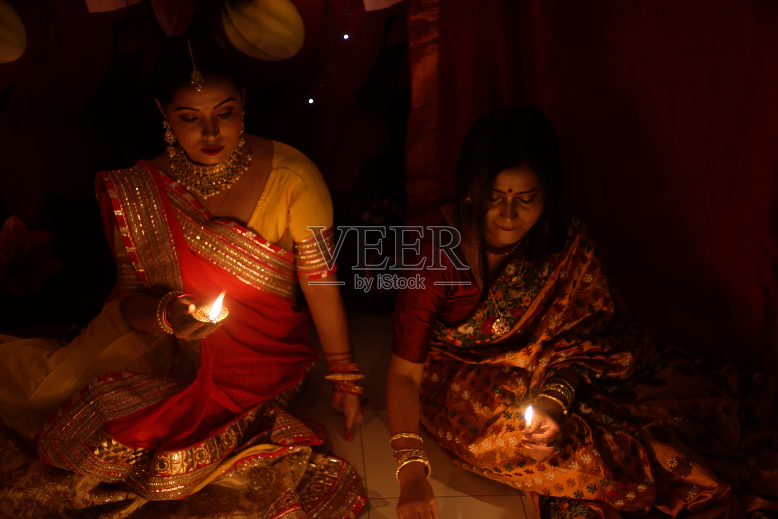 在排灯节的晚上,两名穿着印度传统服装的美丽印度孟加拉妇女坐在室内地板上点亮灯。照片摄影图片